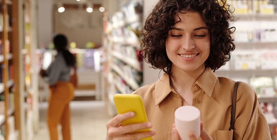 Smiling woman in beige shirt examining her skin